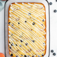 overhead shot of peach and blueberry coffee cake in a pyrex pan with fresh peaches and blueberries scattered in the background