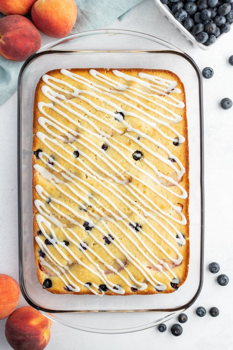 overhead shot of peach and blueberry coffee cake in a pyrex pan with fresh peaches and blueberries scattered in the background