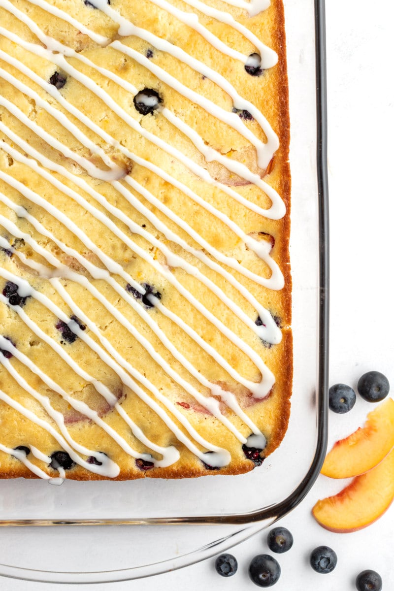 overhead shot of peach and blueberry coffee cake in a pyrex pan with fresh peaches and blueberries scattered in the background