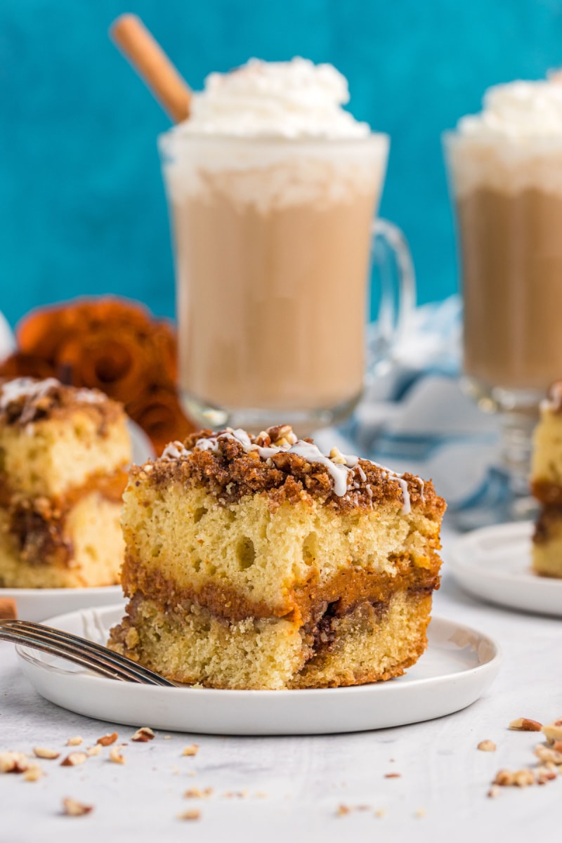 slice of pumpkin coffee cake on a plate with coffee drinks in the background