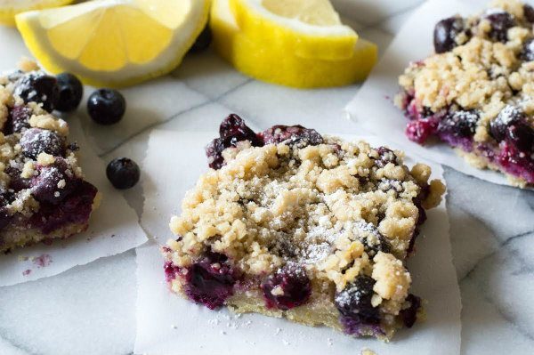 Blueberry Lemon Crumb Bars sitting on parchment paper with fresh cut lemons in the background