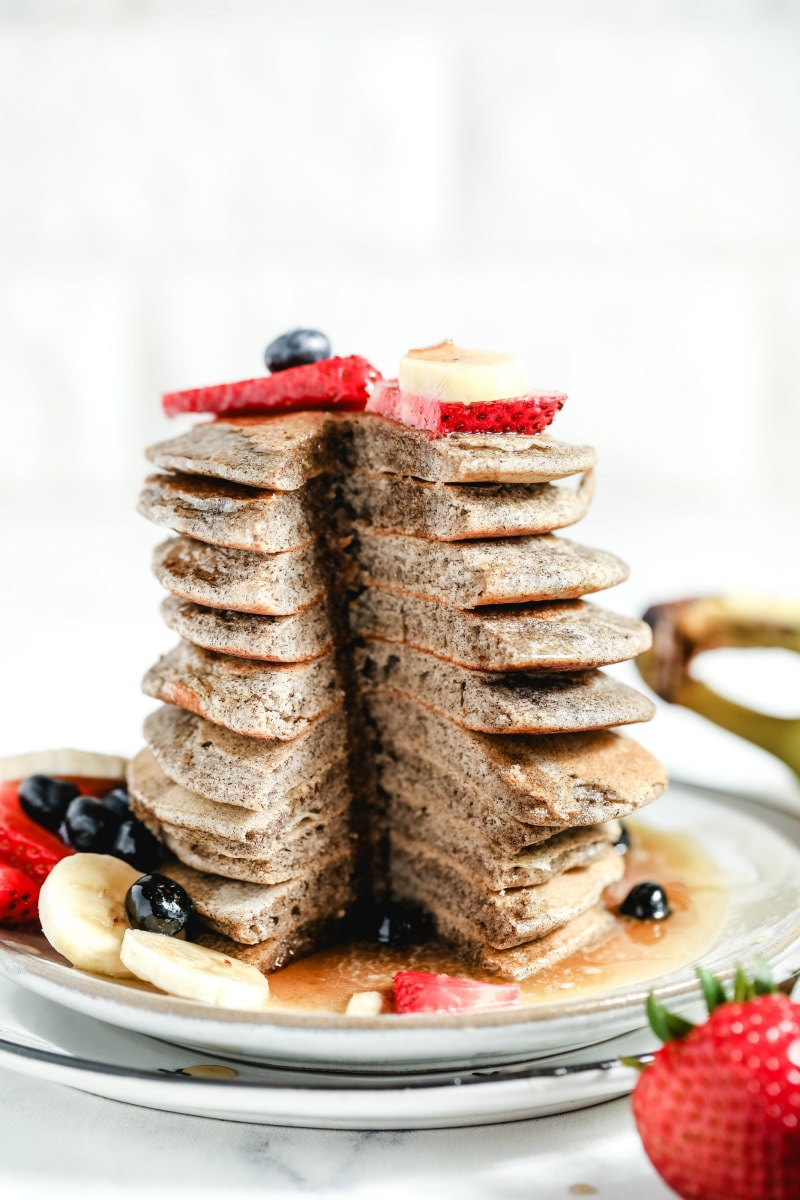 a tall stack of buckwheat pancakes cut into to see the inside, garnished with fresh berries and bananas