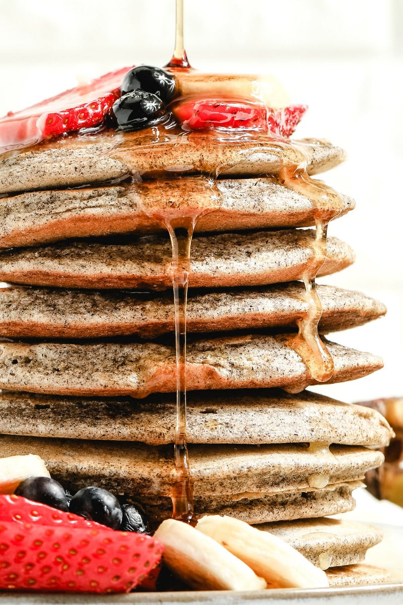 syrup falling down the sides of a stack of buckwheat pancakes garnished with fresh berries