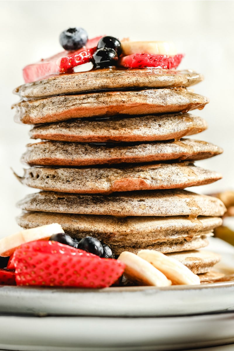 stack of buckwheat pancakes on a white plate, garnished with fresh berries and bananas