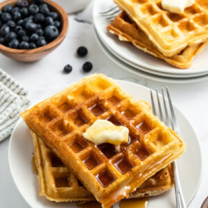 waffles stacked on plate with butter and syrup