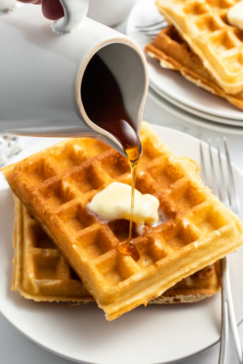 pouring syrup onto stack of waffles