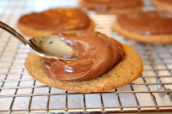 spreading chocolate icing on maple cookies