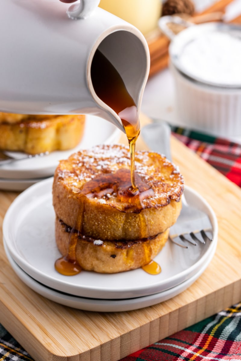 pouring syrup onto two slices eggnog french toast