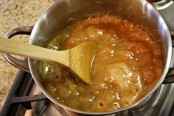 wooden spoon stirring ingredients in pan to create toffee for almond roca