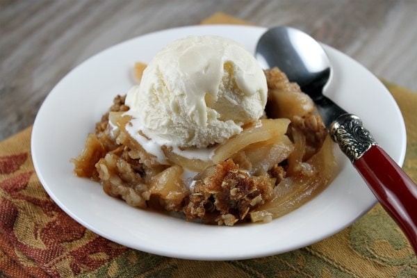 apple crisp topped with ice cream in a white bowl with a spoon