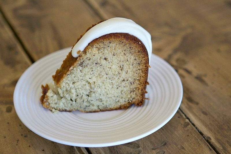 slice of banana bundt cake on a white plate set on a wood background