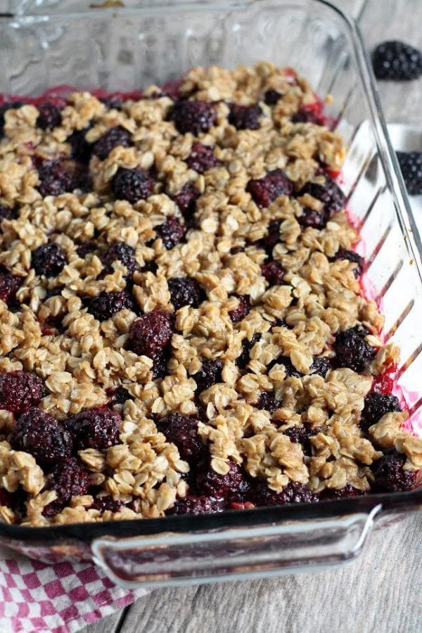pan of blackberry crisp set on top of a white and red checkered cloth napkin with some fresh blackberries in the background