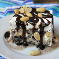 one slice of buster bars on a white plate and topped with fudge and peanuts. displayed on a blue/teal/white striped napkin