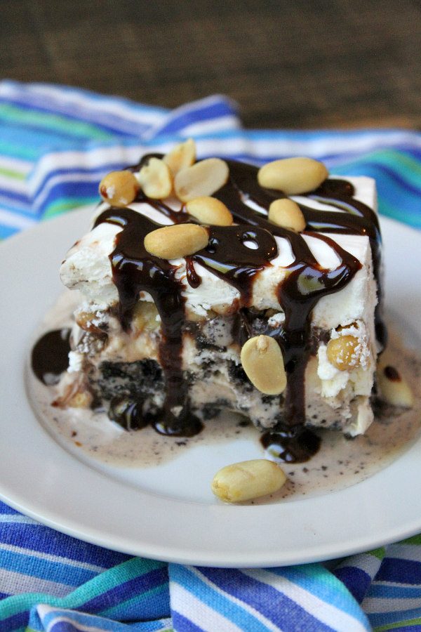 Dairy Queen Buster Bar slice on a white plate, topped with fudge and peanuts. Displayed on blue/teal/white striped napkin.