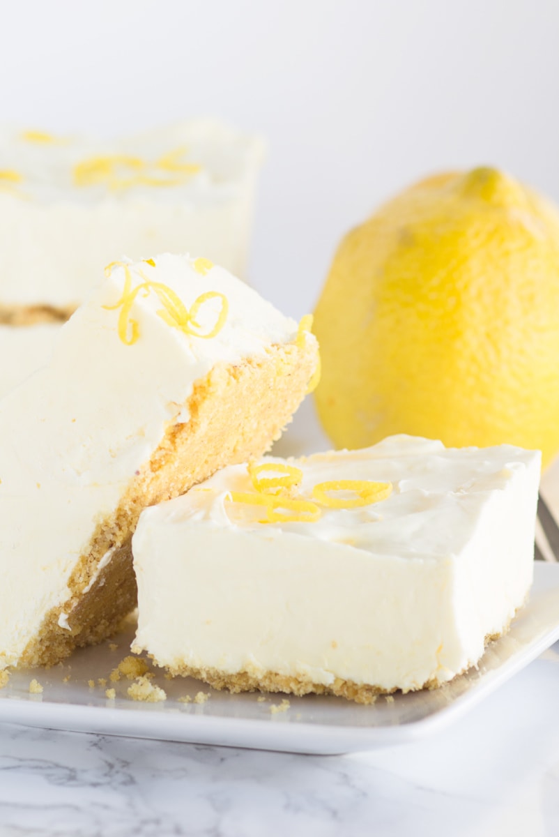 frozen lemon cheesecake squares displayed on white plate with a lemon