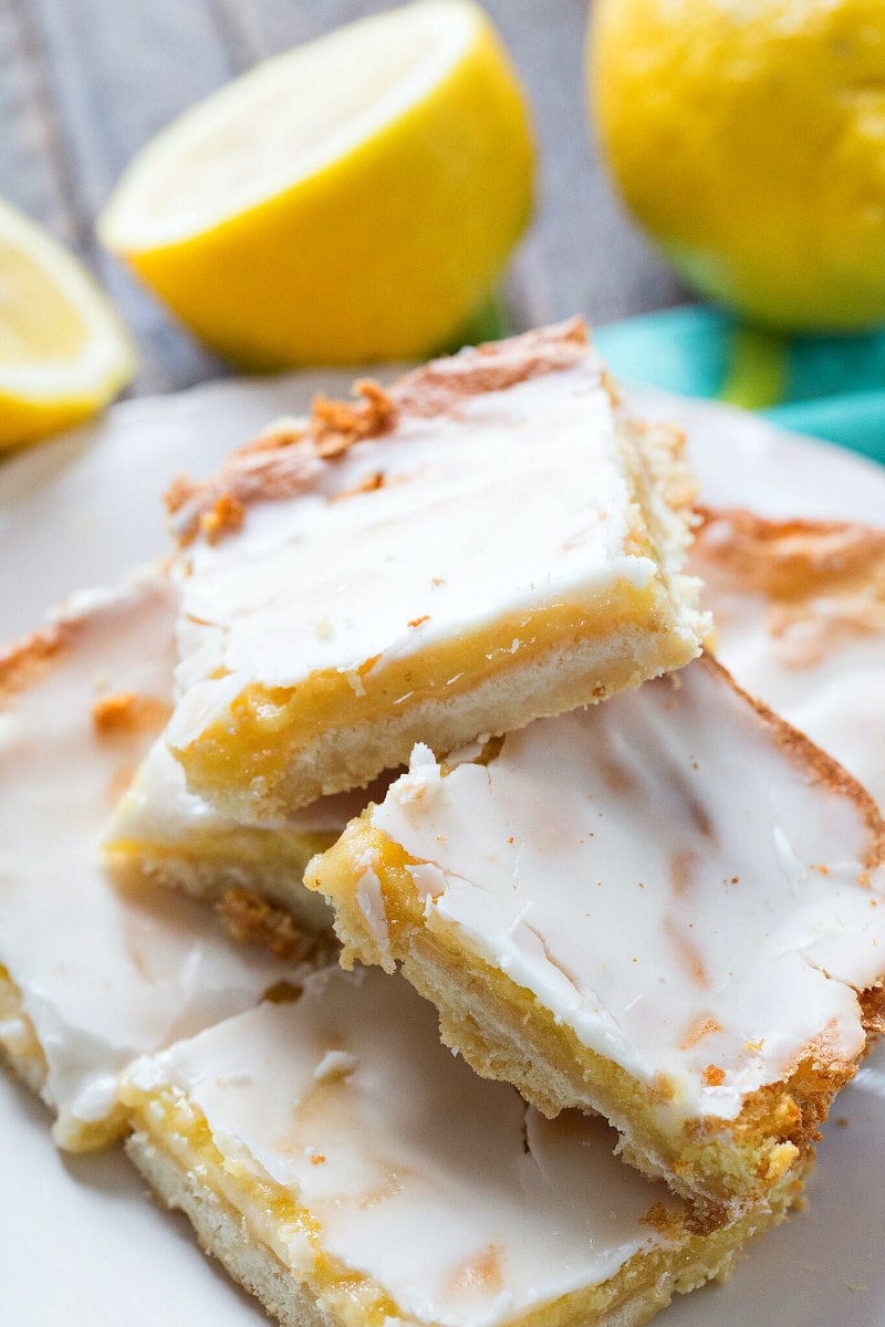 Stacked Lemon Bars displayed on a white plate with fresh lemons in the background