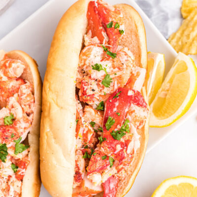 two lobster rolls on plate with lemon wedges