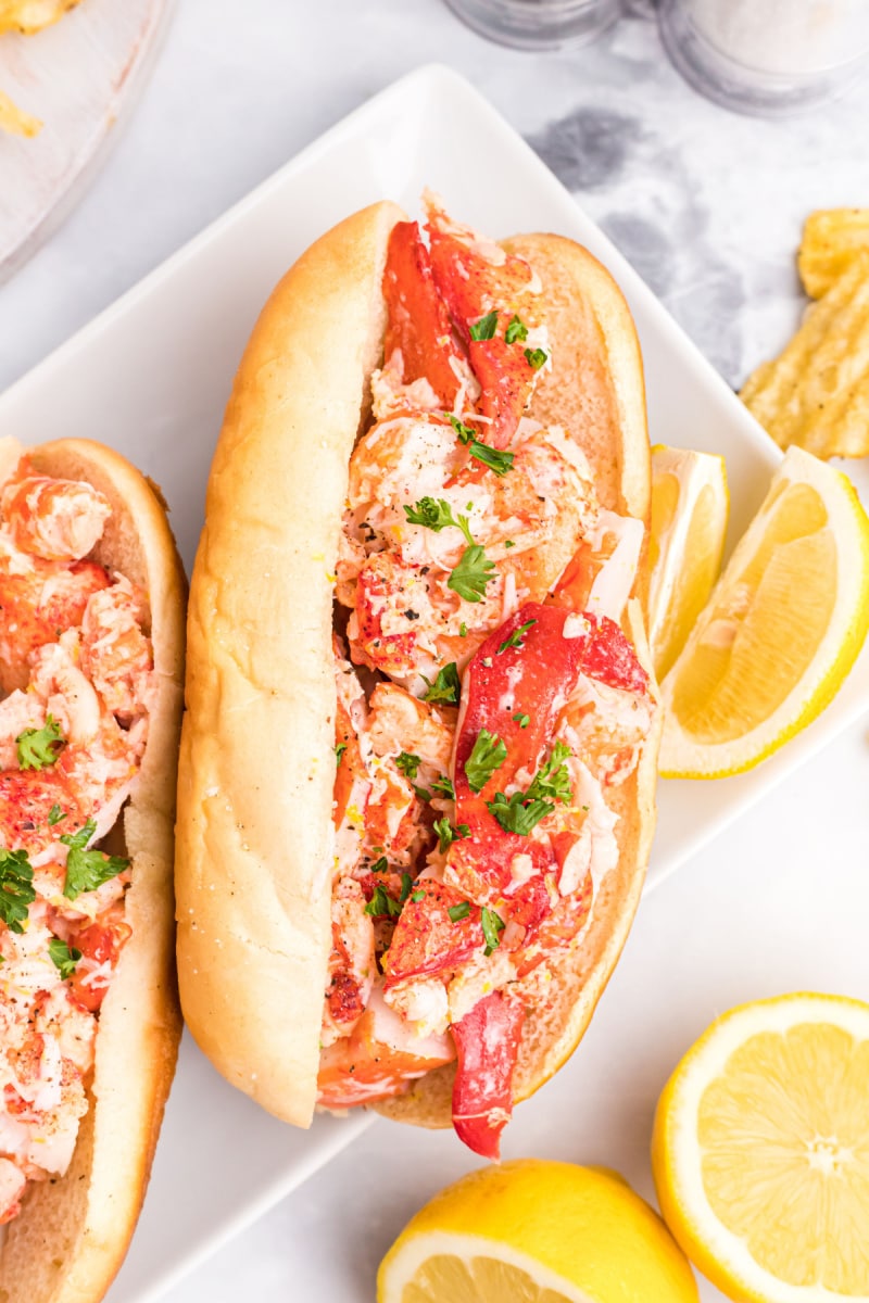 two lobster rolls on plate with lemon wedges