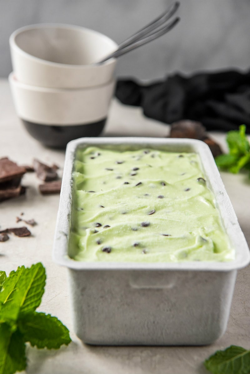 metal container of low fat mint chocolate chip ice cream sitting on the counter with serving dishes in the background and mint leaves as garnish decor