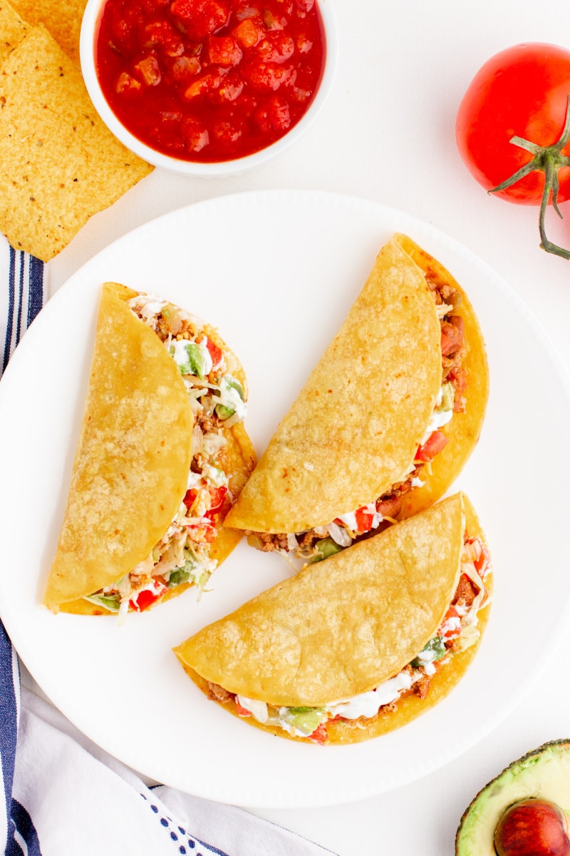 three tacos on a white plate with side of salsa