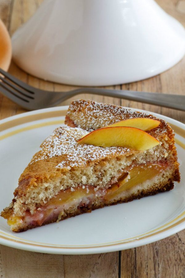 Slice of Nectarine Coffee Cake on a white plate with a yellow stripe around the edge. Fork behind the plate