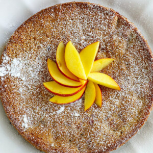 overhead shot of nectarine coffee cake displayed on a white plate with sliced nectarine on top