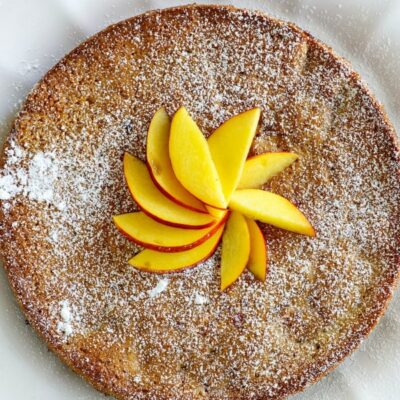 overhead shot of nectarine coffee cake displayed on a white plate with sliced nectarine on top