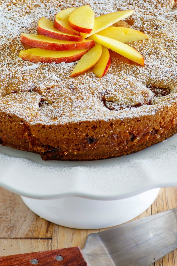 Nectarine Coffee Cake displayed on a white serving platter with fresh nectarines on top. serving spatula alongside.