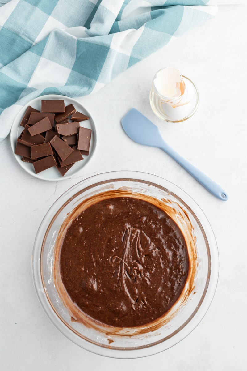 bowl of brownie batter with bowl of chopped chocolate in the background and a blue/white checked napkin