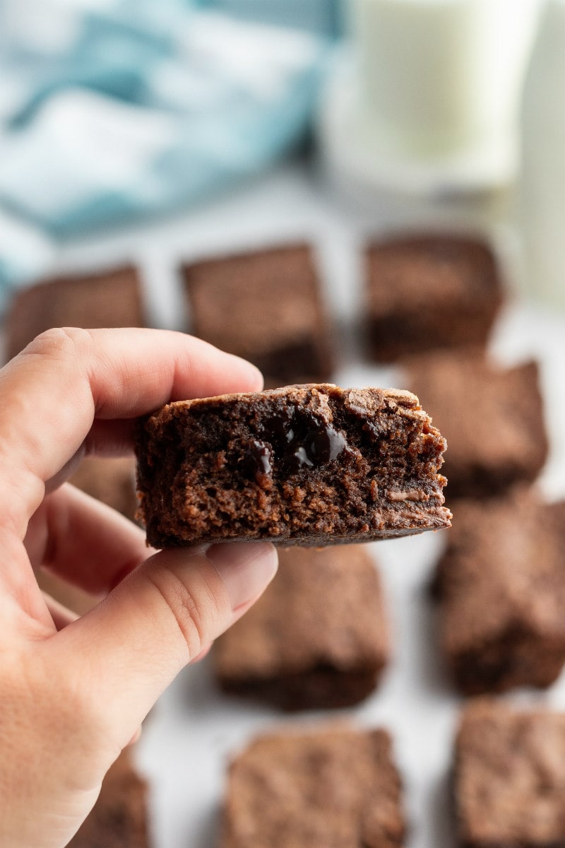 hand holding an ooey gooey brownie with more brownies in the background