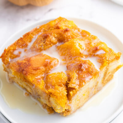 slice of pumpkin bread pudding with bourbon cream sauce on a white plate