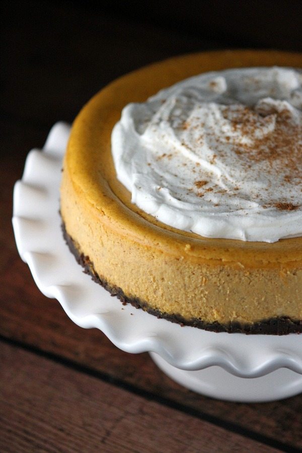 Pumpkin Cheesecake topped with whipped cream on a white cake platter