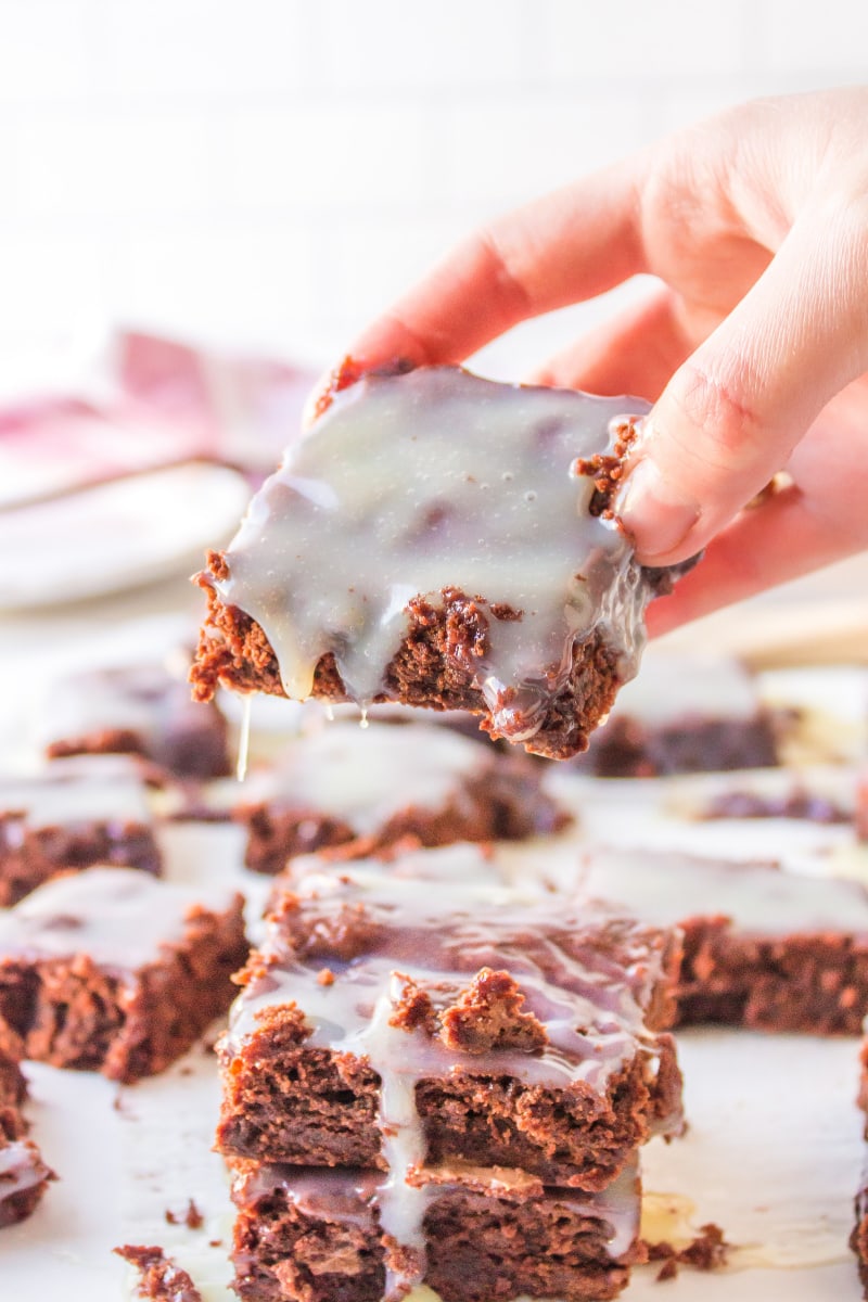 hand picking up a brownie dripping with white chocolate ganache