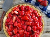 overhead shot of strawberry pie with blue/white checked napkin and fresh strawberries in background