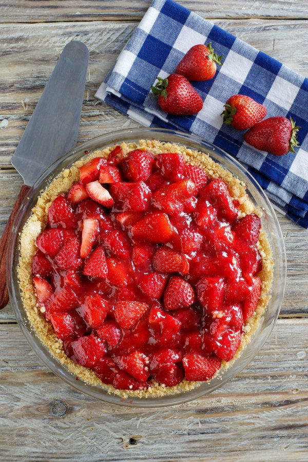 overhead shot of Fresh Strawberry Pie with serving spatula and blue and white checked napkin with fresh strawberries on top