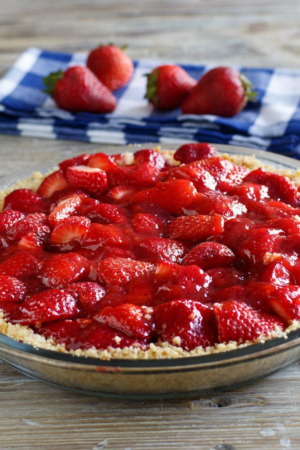 Fresh Strawberry Pie in a glass pie dish. blue and white checked napkin with fresh strawberries on top.