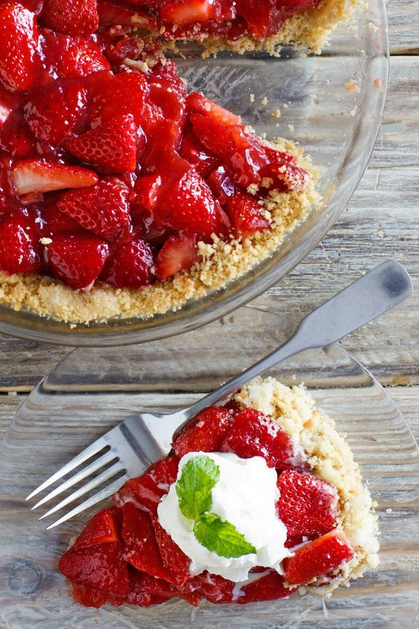 overhead shot of Slice of Fresh Strawberry Pie with whipped cream and fresh mint and a fork. the rest of the pie is in the background