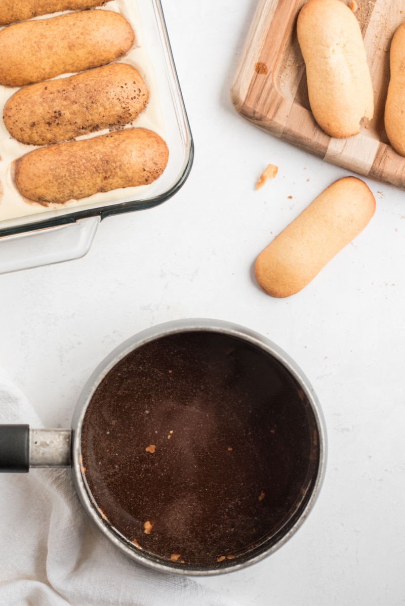 showing process of making tiramisu dipping ladyfingers in coffee and putting in pan