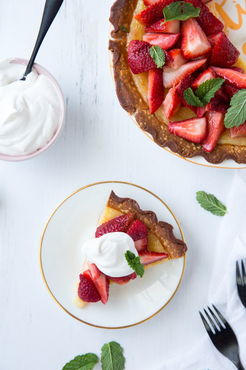 overhead shot of a corner of strawberry lemon buttermilk pie with a slice of pie on a white plate topped with whipped cream