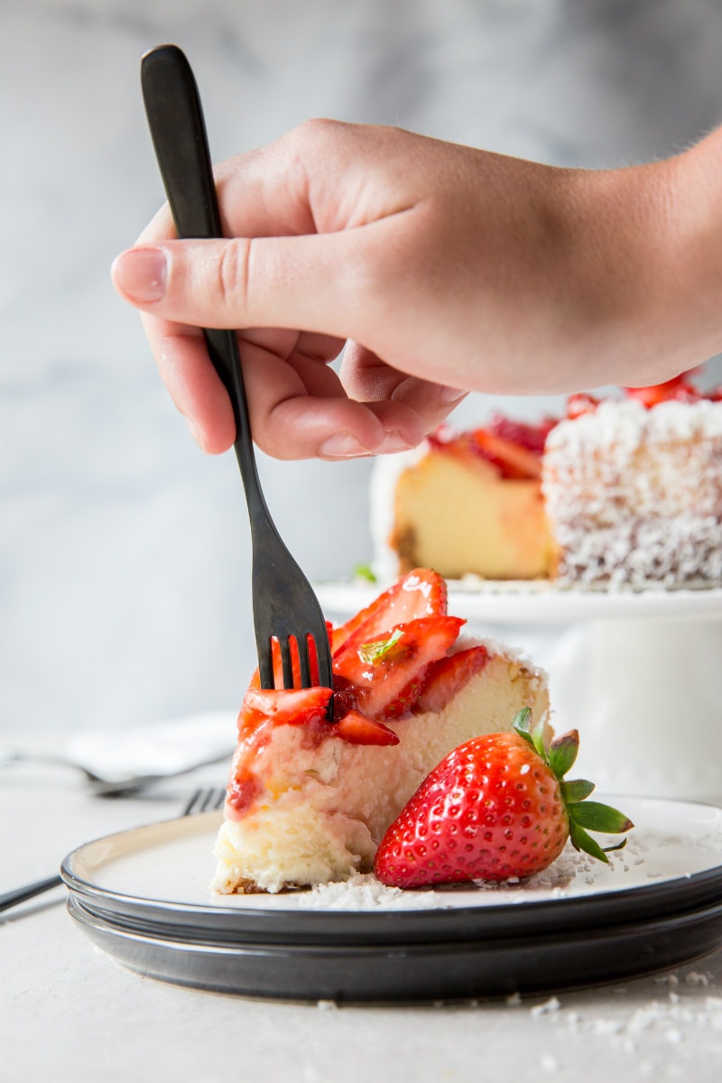 slice of strawberry coconut cheesecake- hand with fork taking a bite