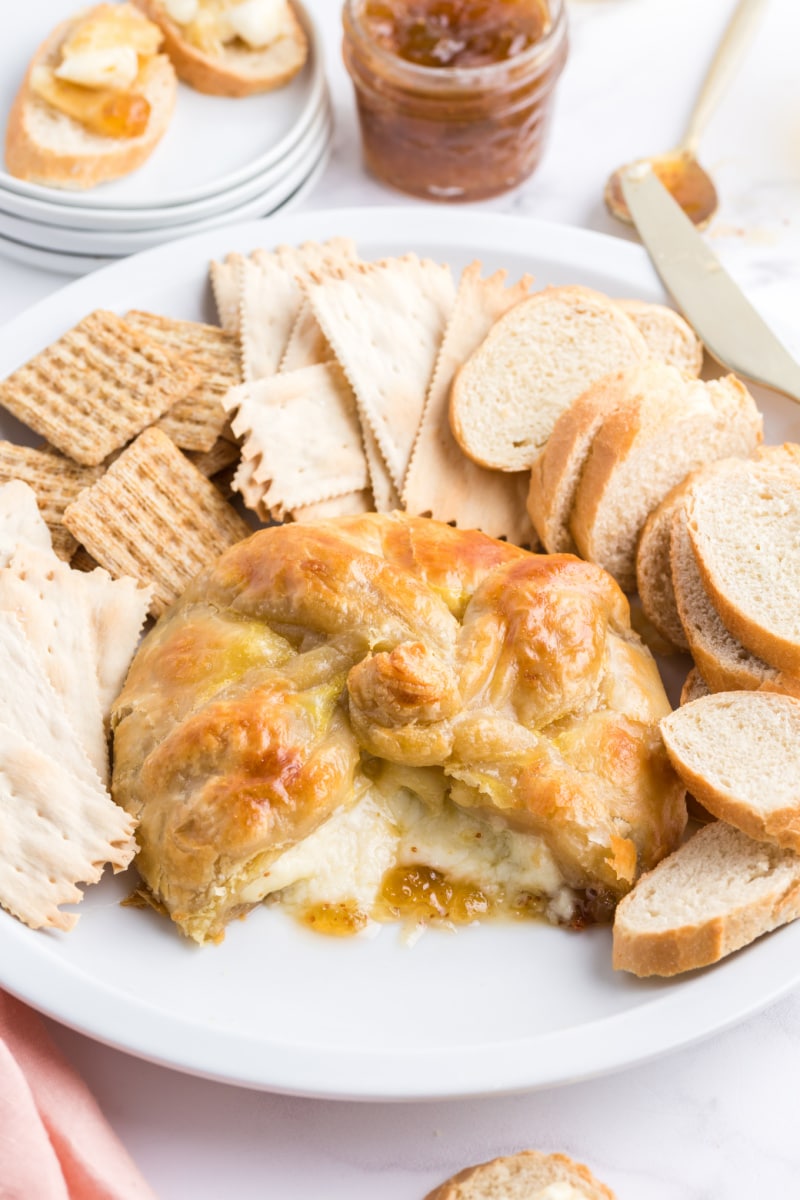 baked brie with fig jam displayed on plate with crackers and baguette