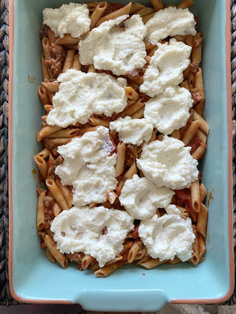 making baked penne with italian sausage showing adding ricotta to the pasta in the casserole dish