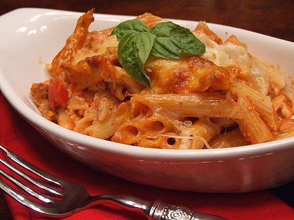 serving of baked penne with Italian sausage in a white dish with fresh basil garnish