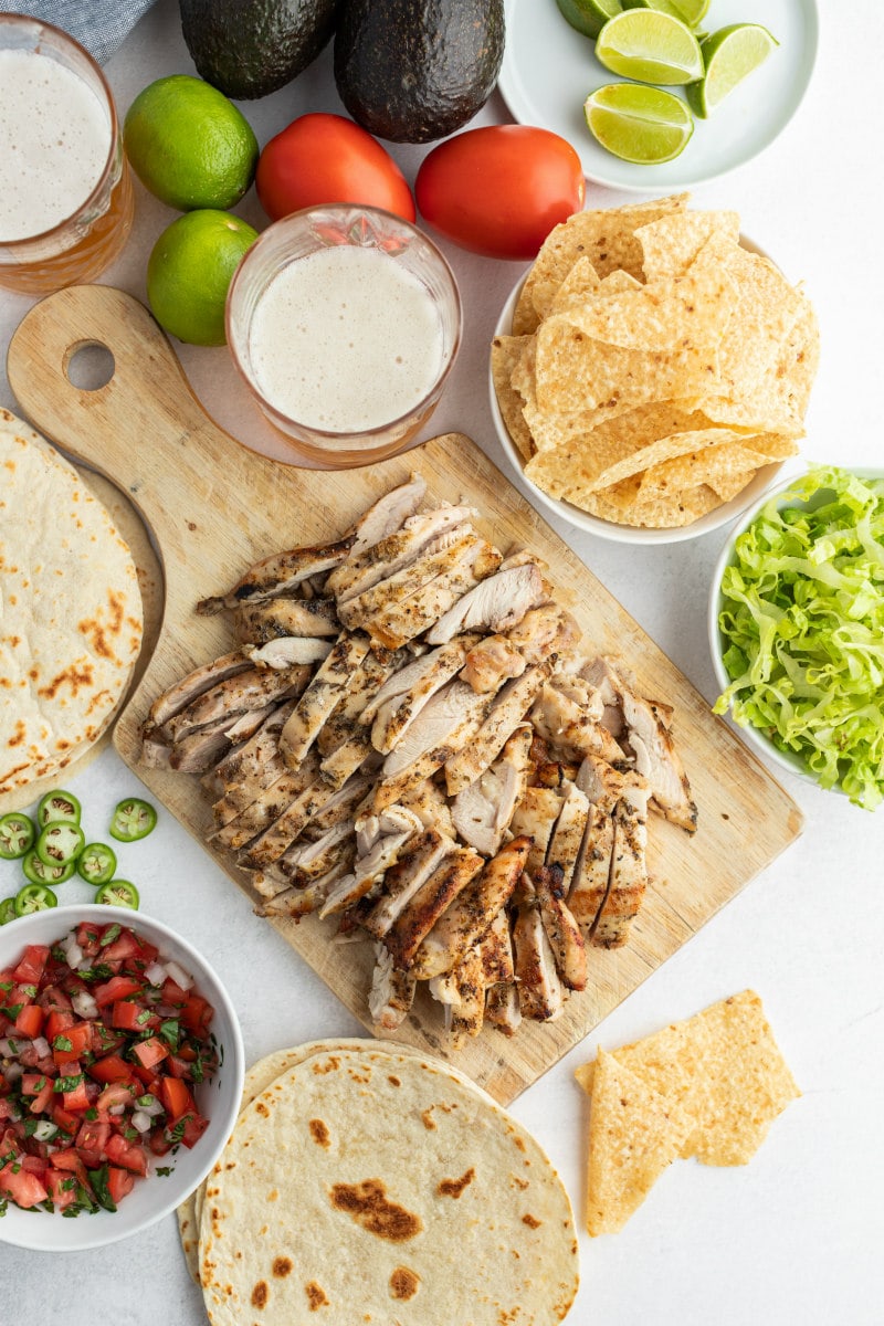 chopped chicken for tacos on wood board surrounded by bowls of taco fixings