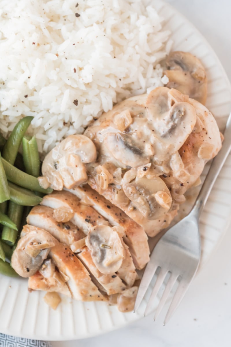 sliced chicken breast on a plate with mushroom sauce and rice and beans