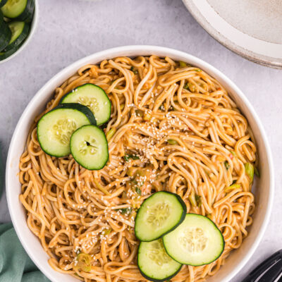 cold sesame noodles in a bowl with cucumber slices