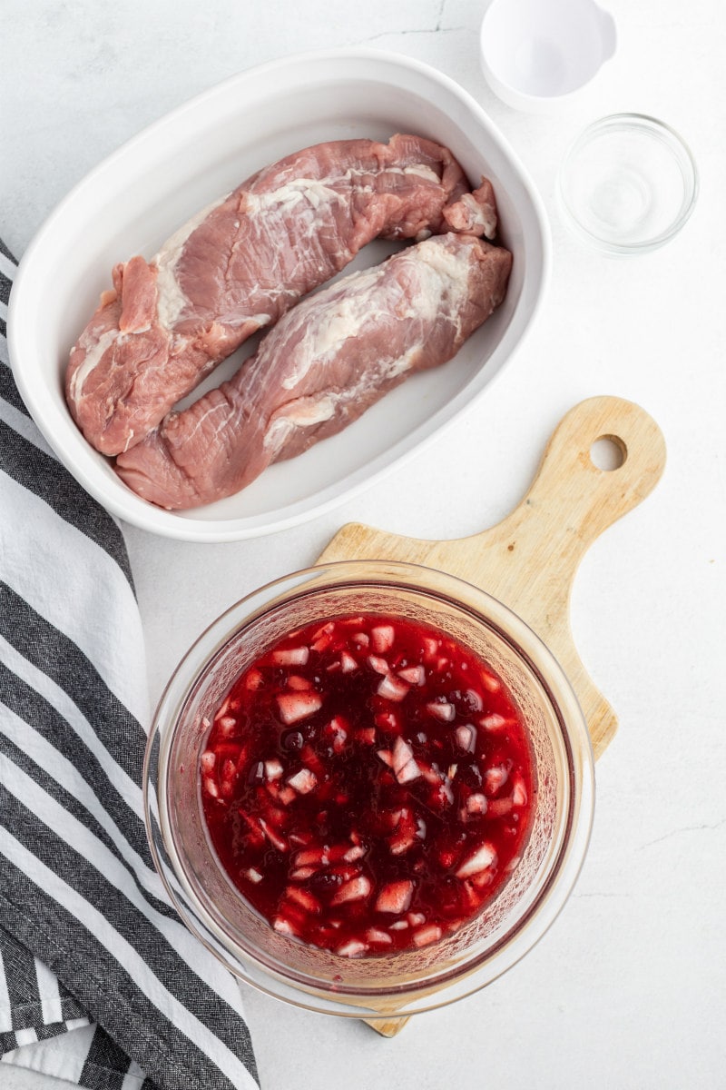 pork tenderloin in white casserole dish and cranberry sauce on the side