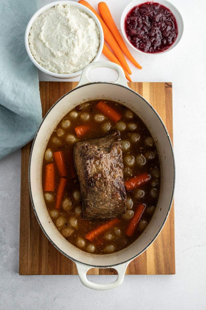 cranberry roast beef in Dutch oven surrounded by carrots and onions