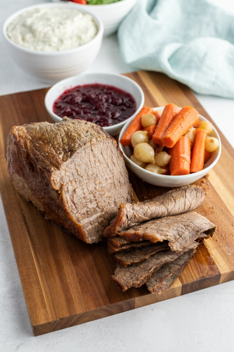 cranberry roast beef sliced on cutting board with vegetables and cranberry sauce