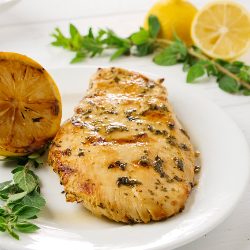 grilled chicken with lemon and oregano on a white plate with a grilled lemon and fresh oregano and fresh cut lemons